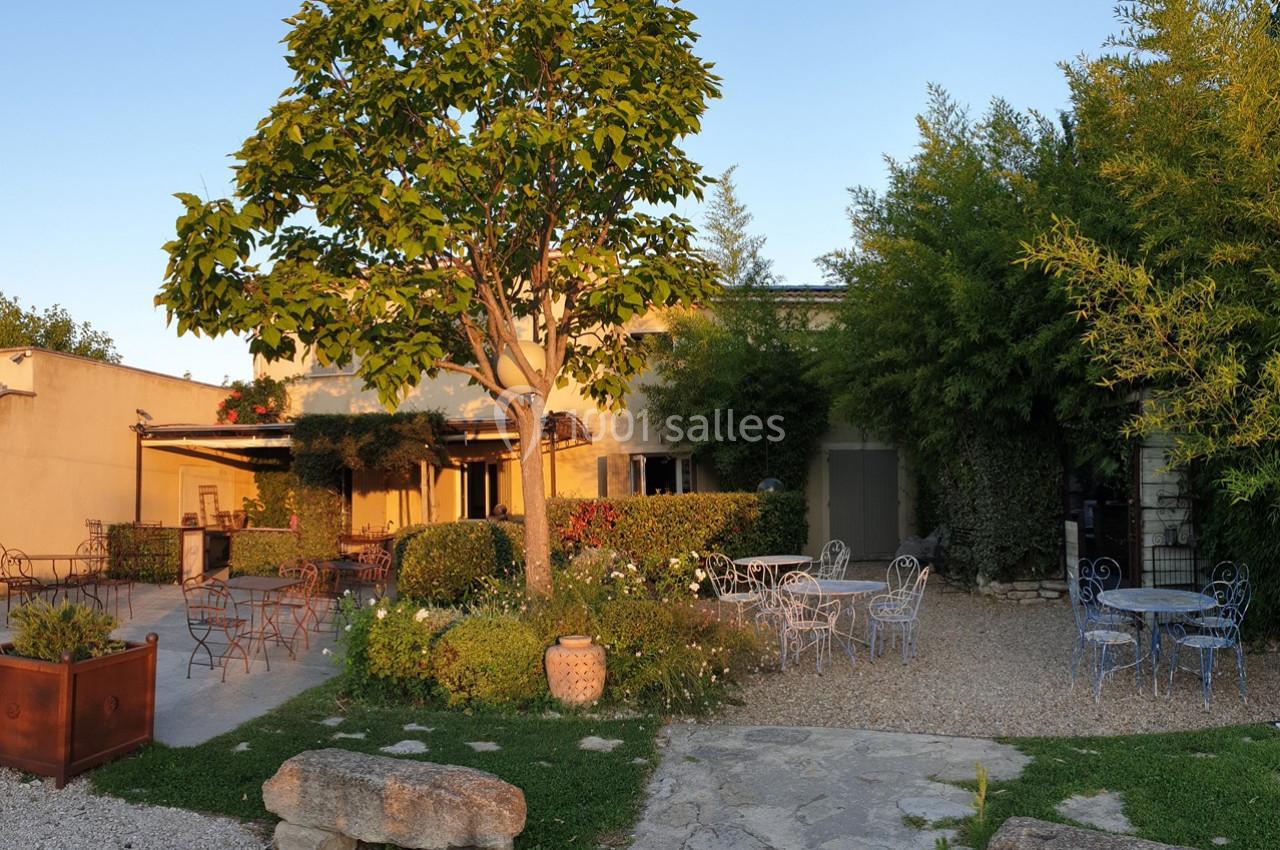Cour extérieure avec mobilier en fer forgé, végétation abondante et lumière douce en fin de journée.