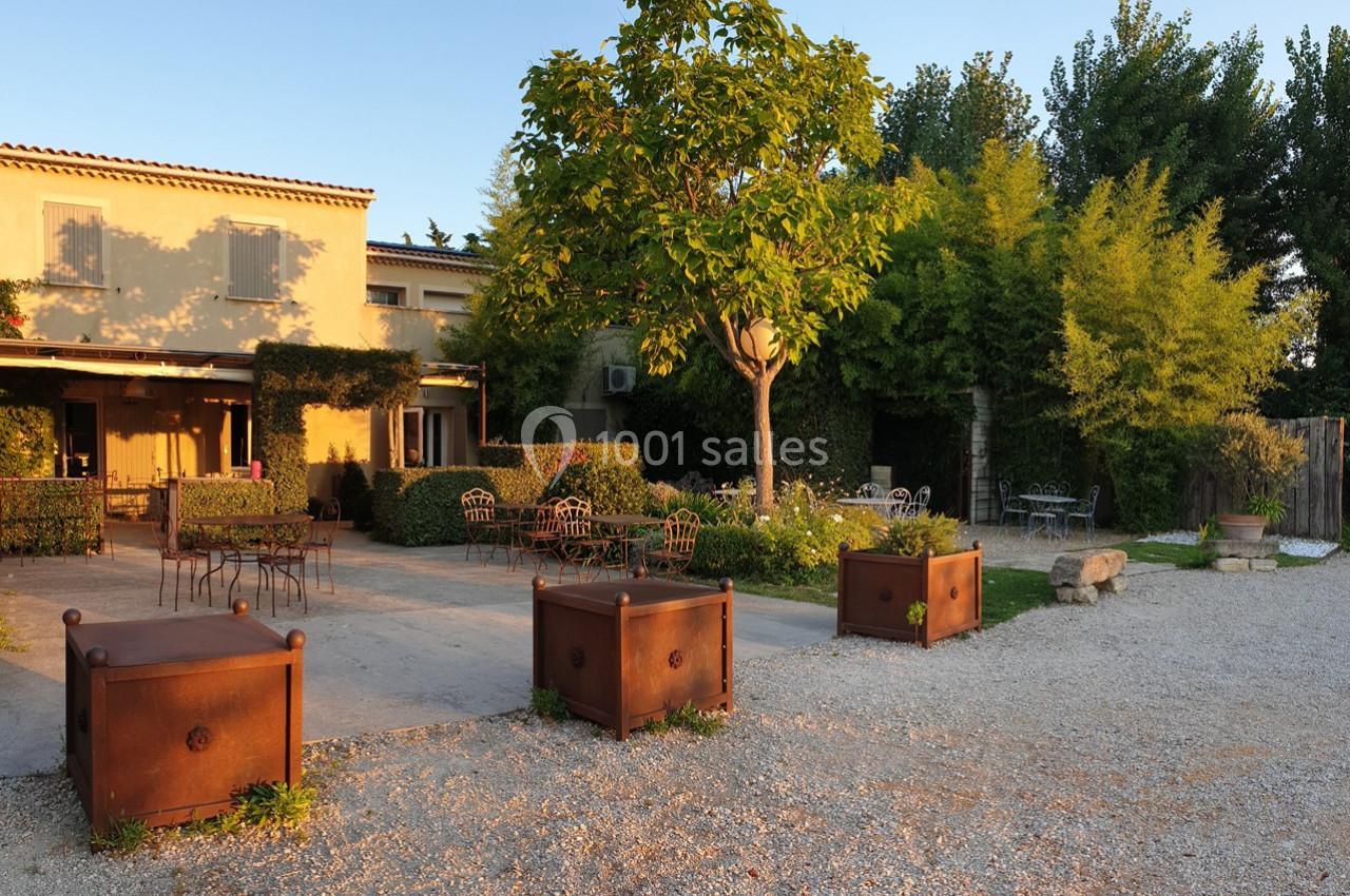 Terrasse ensoleillée avec tables et chaises en métal, entourée de verdure et de bacs de plantation en bois.