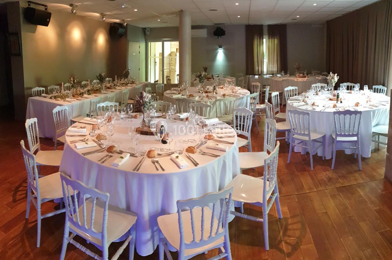 Salle de réception avec tables rondes et rectangulaires dressées pour un événement, décorée de manière élégante.
