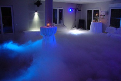 Salle avec parquet, tables basses, fauteuils en cuir sombre, comptoir rouge au fond et ambiance tamisée.