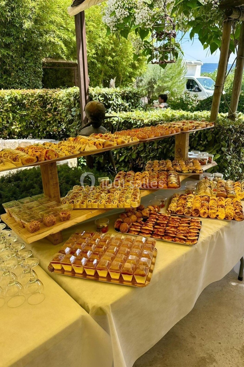 Buffet en extérieur avec une variété de viennoiseries et pâtisseries disposées sur des étagères en bois.