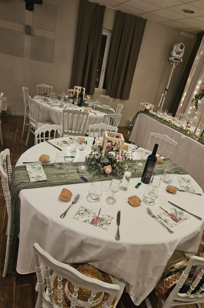 Tables rondes décorées pour un événement, avec nappes blanches, chemins de table verts et centres de table floraux.