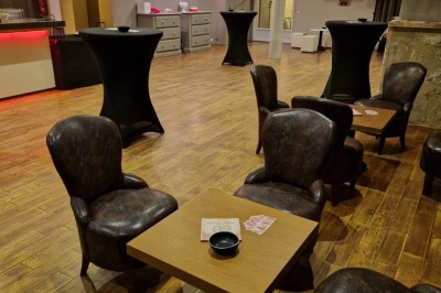 Salle avec parquet, tables basses, fauteuils en cuir sombre, comptoir rouge au fond et ambiance tamisée.