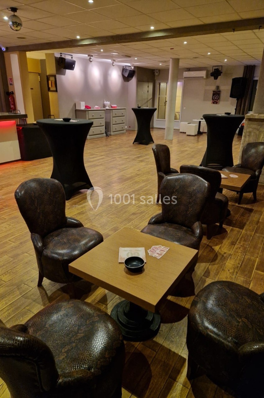 Salle avec parquet, tables basses, fauteuils en cuir sombre, comptoir rouge au fond et ambiance tamisée.