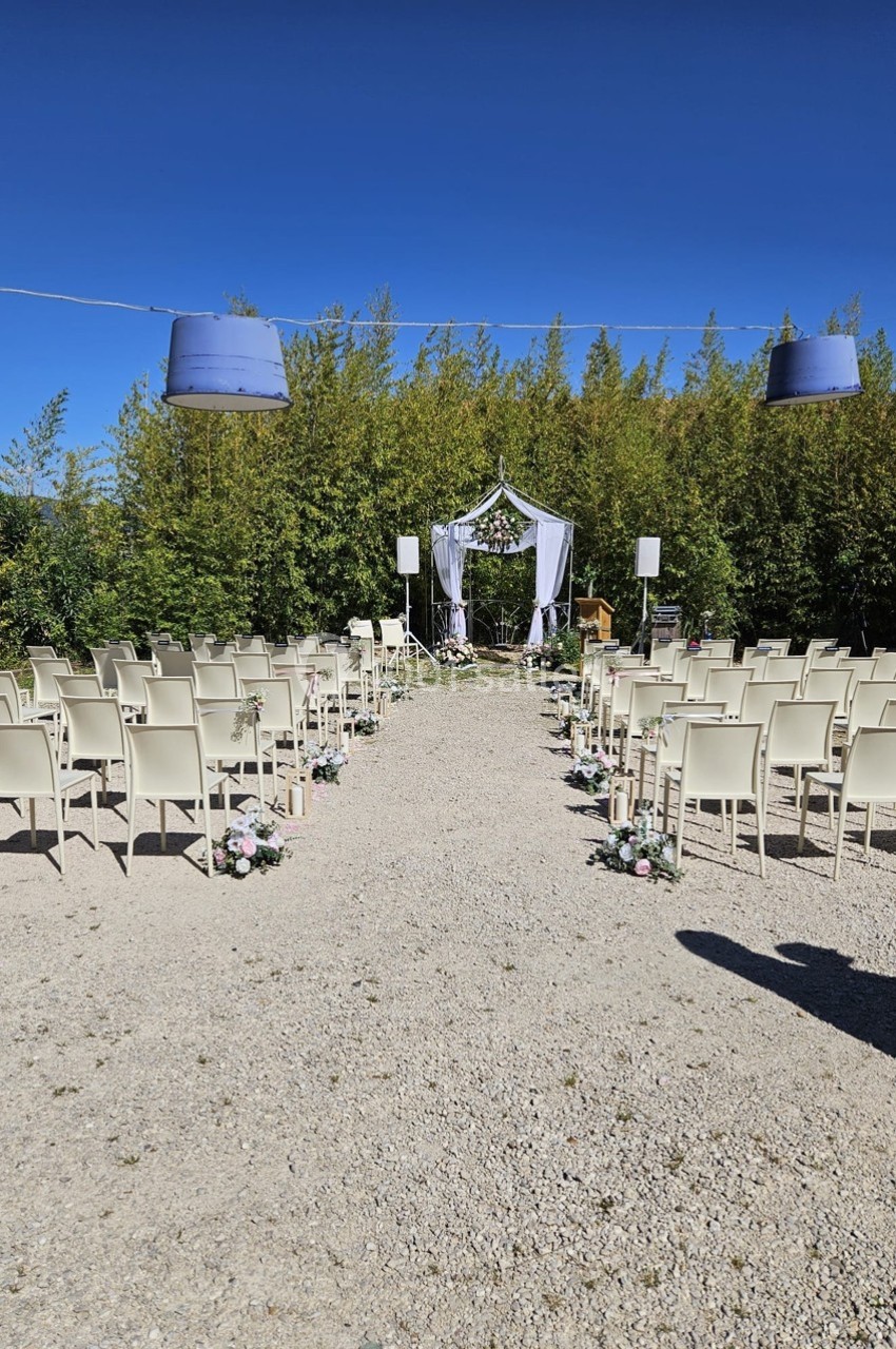 Chaises alignées en extérieur face à une arche décorée pour une cérémonie, entourées de verdure sous un ciel bleu.