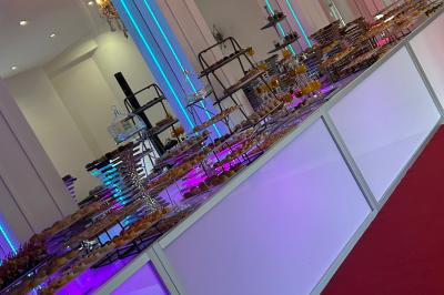 Centre de table décoratif avec bougie, fleurs blanches et roses, entouré de cadeaux sur une table de réception élégante.