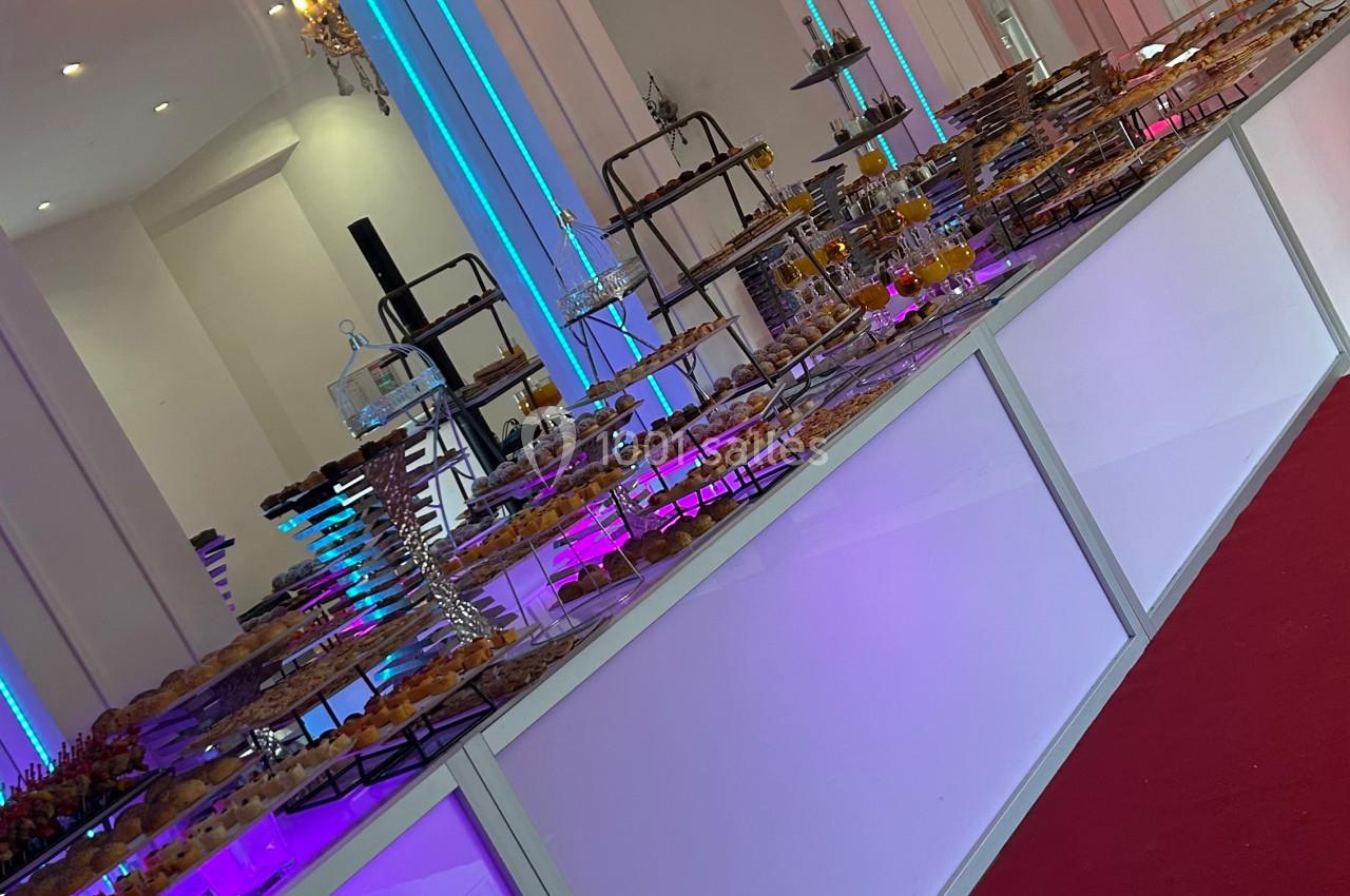 Buffet lumineux avec desserts variés disposés sur des présentoirs dans une salle décorée de lustres et d'arcs éclairés.