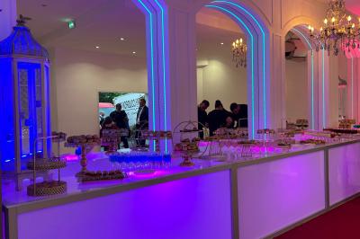 Centre de table décoratif avec bougie, fleurs blanches et roses, entouré de cadeaux sur une table de réception élégante.