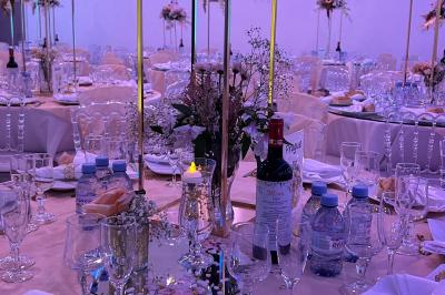 Centre de table décoratif avec bougie, fleurs blanches et roses, entouré de cadeaux sur une table de réception élégante.