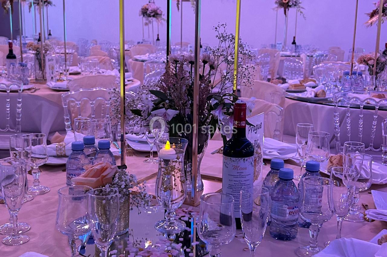 Table de réception élégamment dressée avec nappes roses, décorations florales, couverts dorés et bouteilles sur la table.