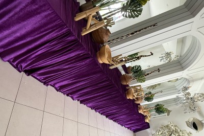Table décorée d'une nappe violette avec des plantes, paniers en osier et éléments en bois, dans une salle lumineuse.