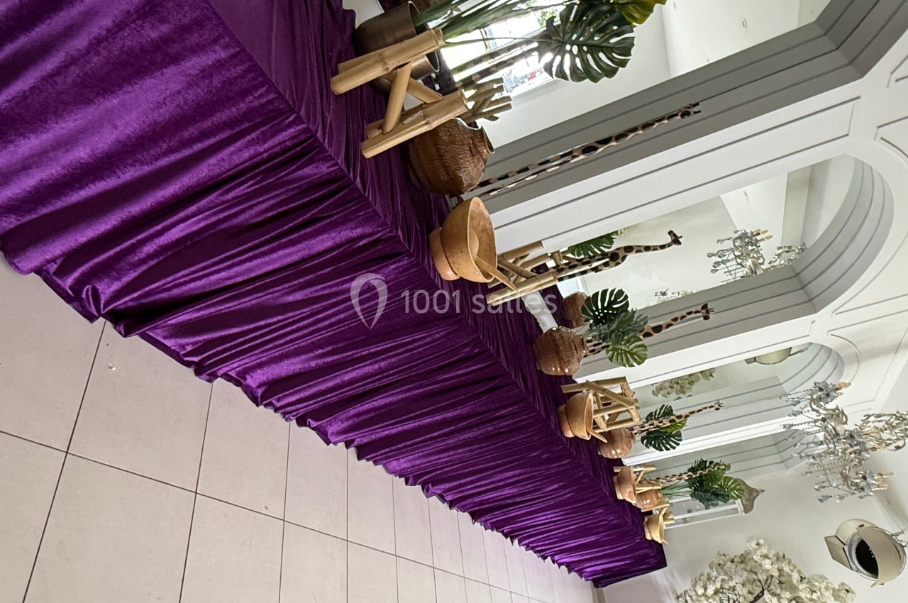 Table décorée d'une nappe violette avec des plantes, paniers en osier et éléments en bois, dans une salle lumineuse.