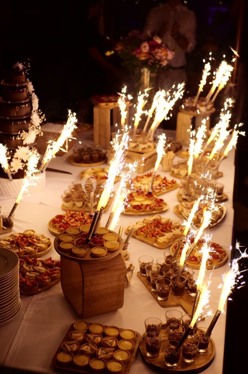 Table garnie de desserts variés et de décorations lumineuses avec des cierges magiques allumés.