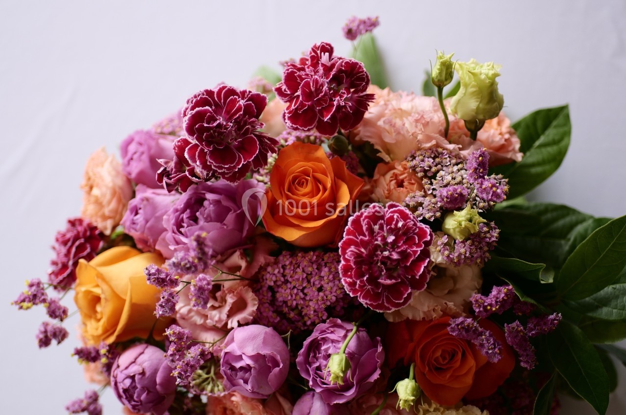 Bouquet de fleurs colorées composé de roses orange, œillets violets, et feuillage vert sur fond clair.