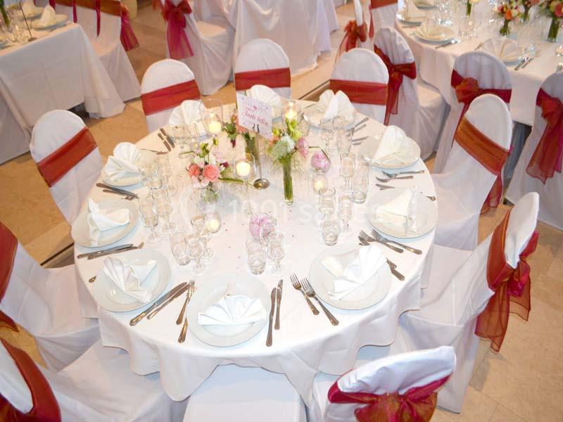 Table ronde dressée pour un événement, avec nappes blanches, serviettes pliées, vaisselle élégante et chaises décorées de…