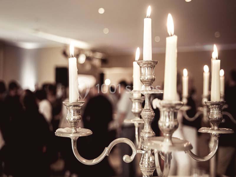 Chandelier en métal argenté avec des bougies allumées, en arrière-plan flou d'une salle avec des personnes.