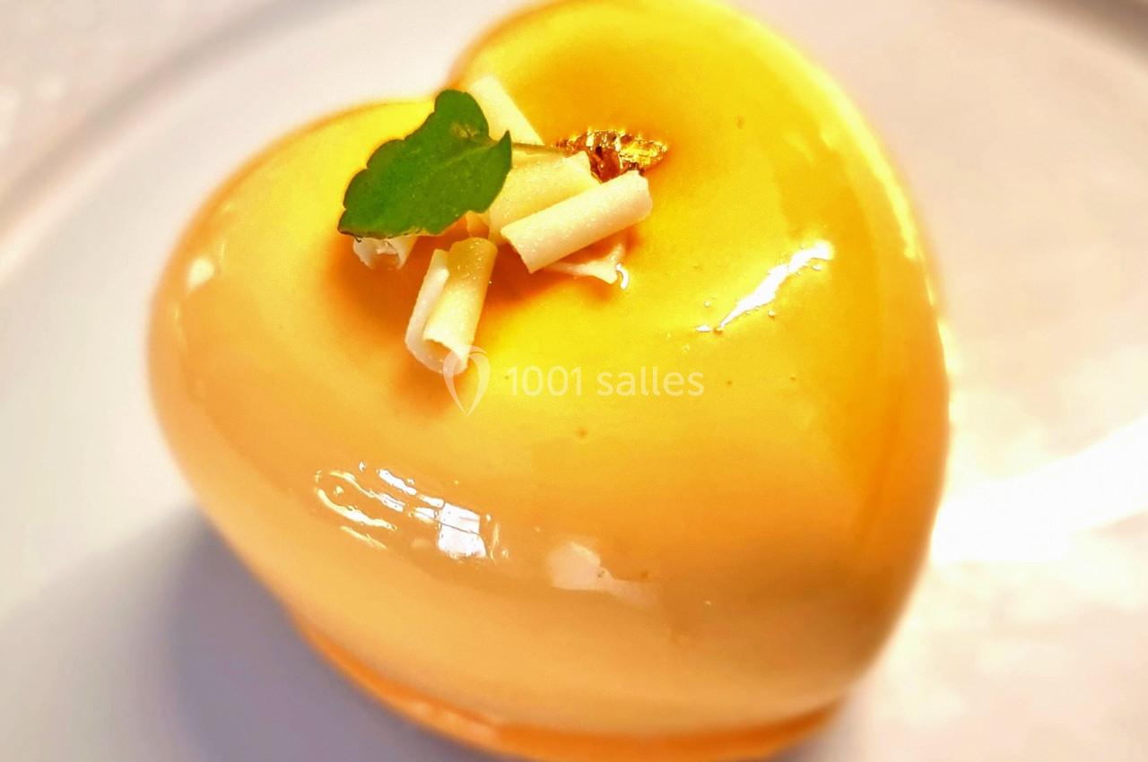 Gâteau en forme de cœur, glaçage jaune brillant, décoré de feuilles et de rouleaux de chocolat blanc.