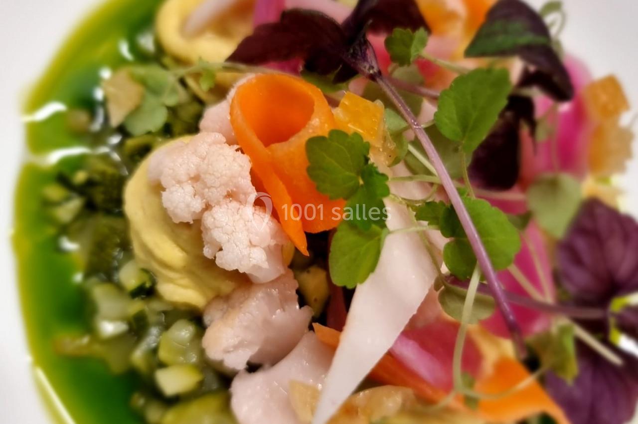 Assiette colorée de légumes variés, incluant carottes, chou-fleur et herbes, présentée sur une sauce verte.
