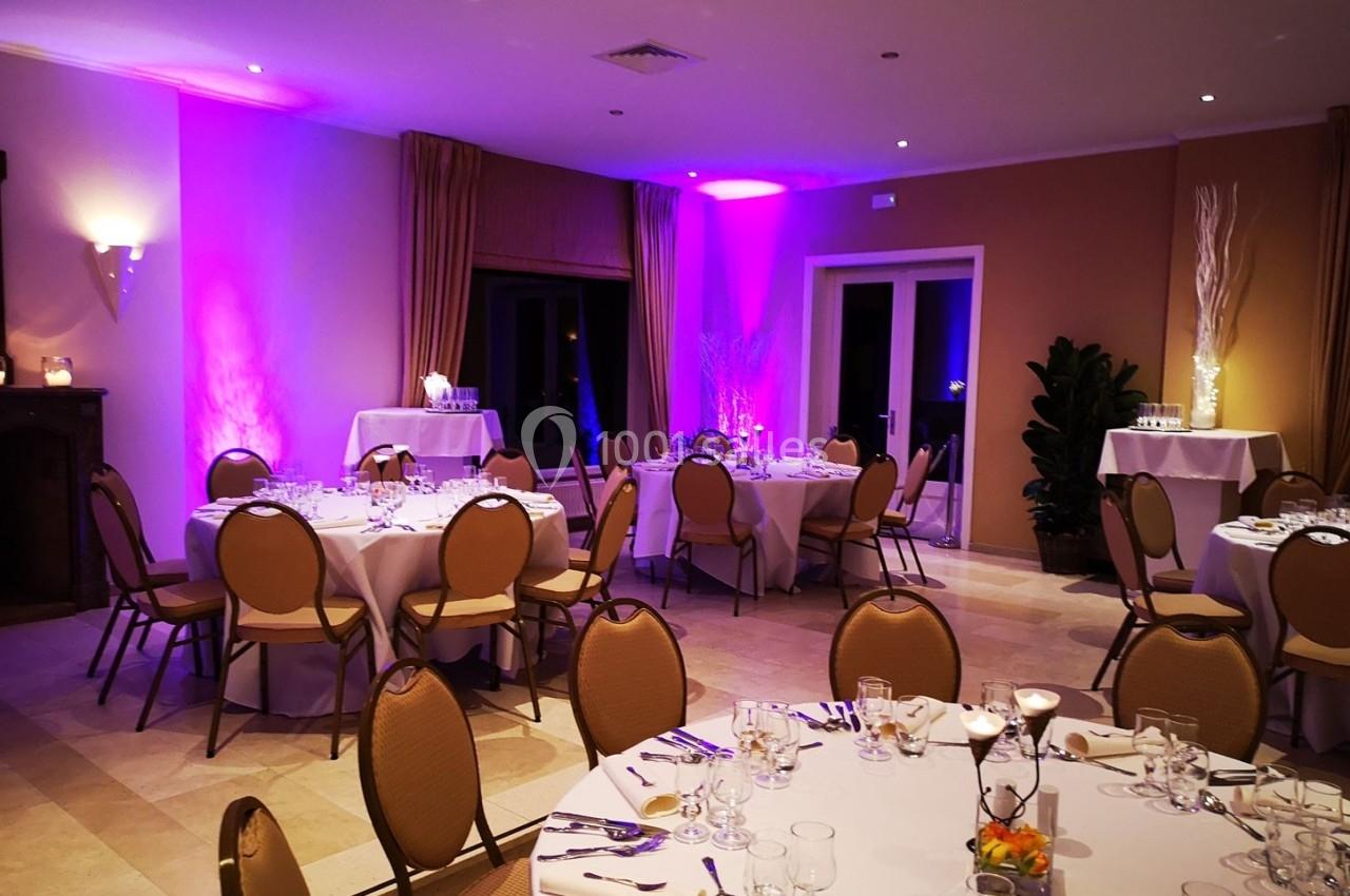 Salle de réception décorée avec des tables rondes dressées, éclairage tamisé et ambiance chaleureuse.