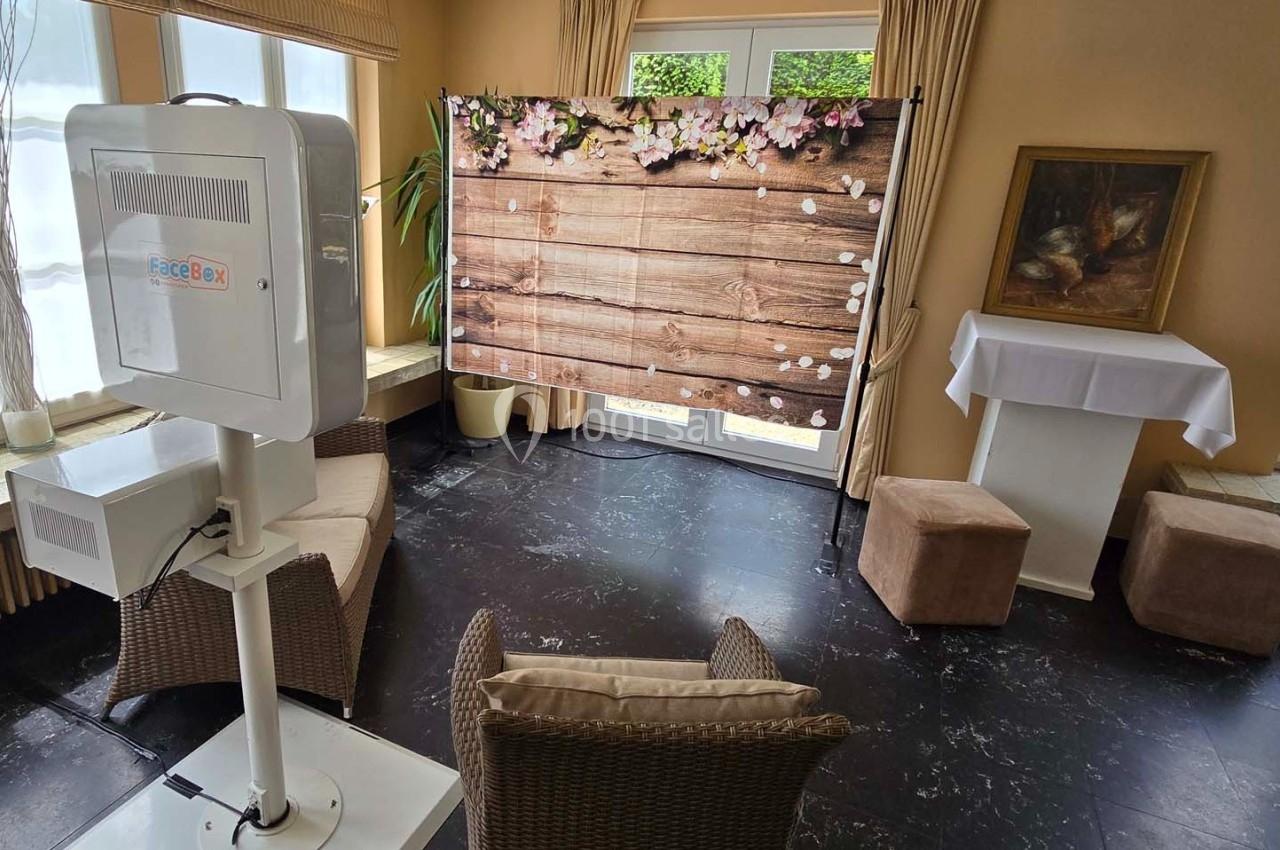 Photobooth installé dans une pièce lumineuse avec un fond en bois décoré de fleurs et des meubles en rotin.