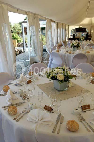 Tables élégamment dressées sous une tente blanche, décorées de fleurs et de vaisselle pour un événement festif.