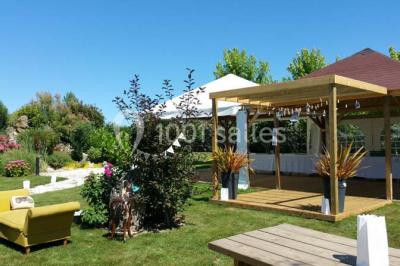 Deux balais déguisés en mariés avec robe et costume, posés devant une tente blanche et un cadre décoratif.