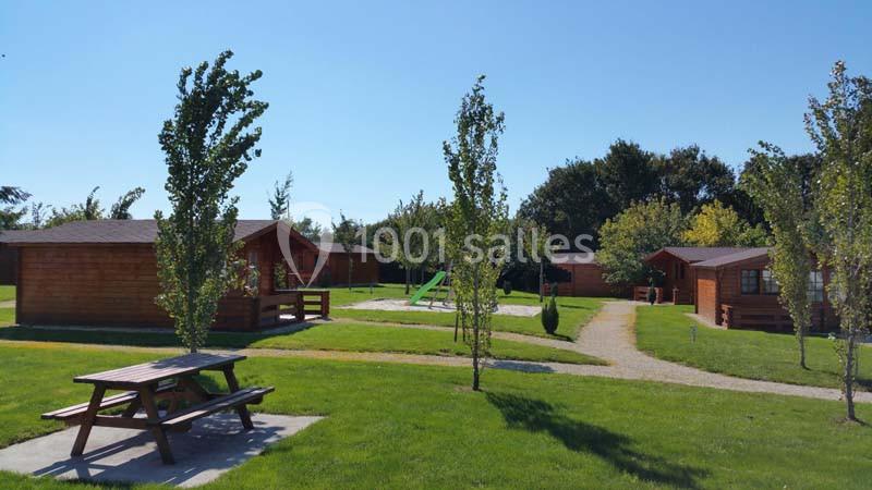 Chalets en bois entourés de pelouses, avec une aire de jeux et des arbres sous un ciel dégagé.