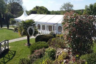 Deux balais déguisés en mariés avec robe et costume, posés devant une tente blanche et un cadre décoratif.