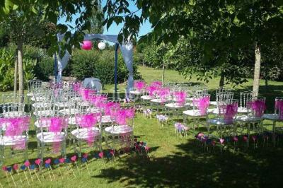 Deux balais déguisés en mariés avec robe et costume, posés devant une tente blanche et un cadre décoratif.