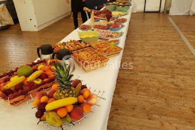 Deux balais déguisés en mariés avec robe et costume, posés devant une tente blanche et un cadre décoratif.