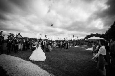 Deux balais déguisés en mariés avec robe et costume, posés devant une tente blanche et un cadre décoratif.