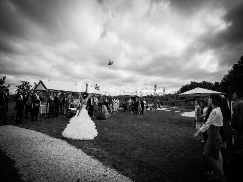 Une mariée lance son bouquet de fleurs vers un groupe d'invités rassemblés dans un jardin lors d'une réception.
