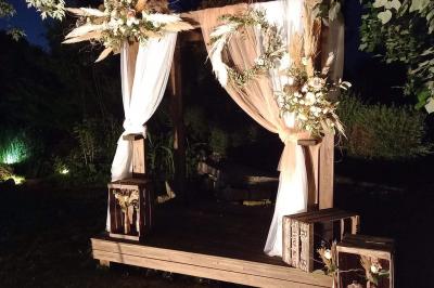 Deux balais déguisés en mariés avec robe et costume, posés devant une tente blanche et un cadre décoratif.