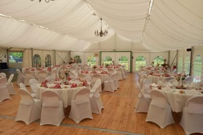 Deux balais déguisés en mariés avec robe et costume, posés devant une tente blanche et un cadre décoratif.