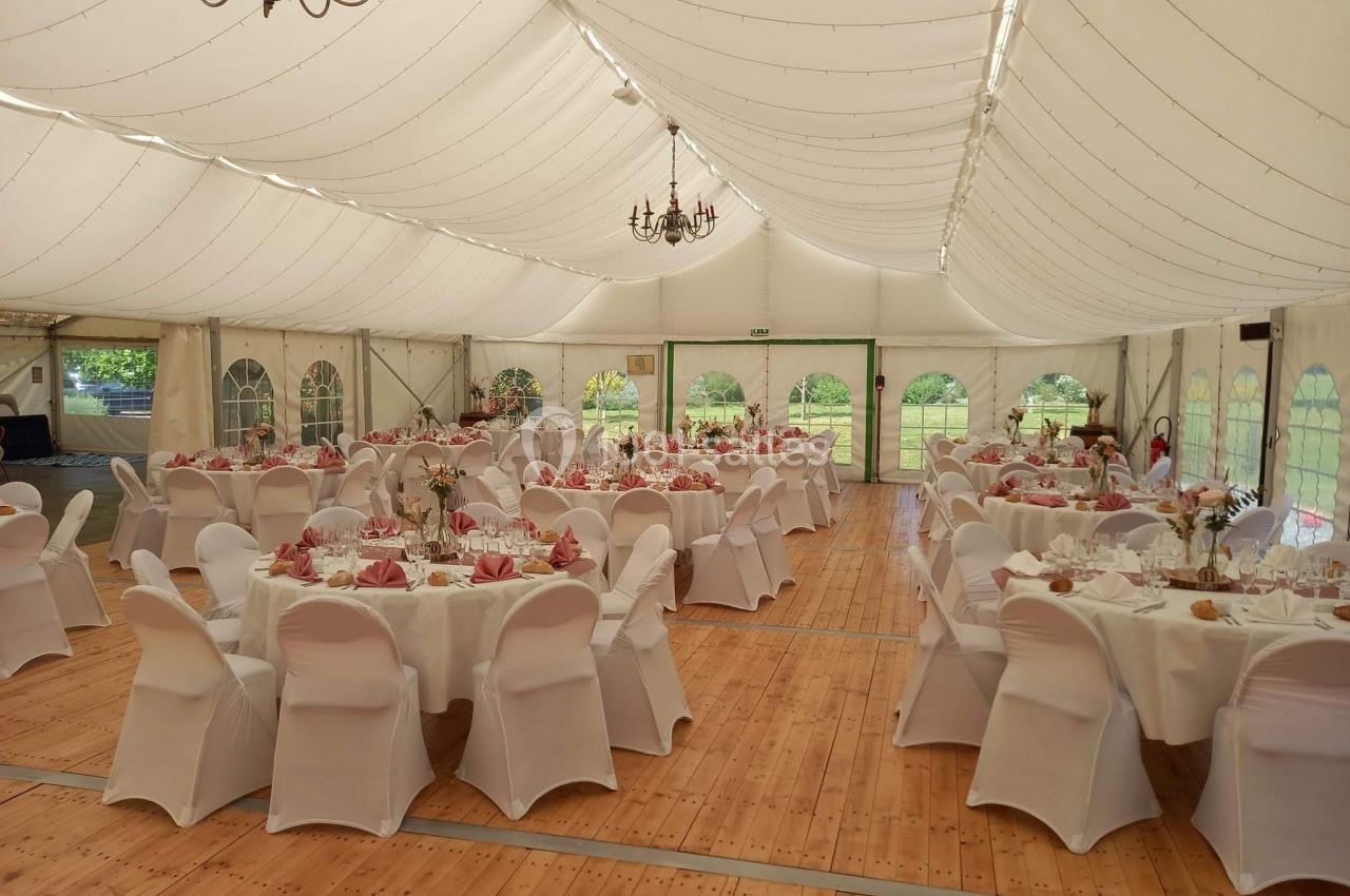 Intérieur d'une tente de réception avec tables rondes dressées, nappes blanches et chaises couvertes, prêt pour un événement.