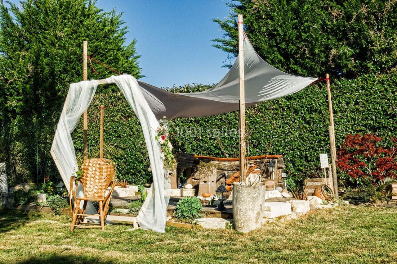 Espace extérieur aménagé avec voile d'ombrage, fauteuil en rotin, décorations florales et mobilier en bois.