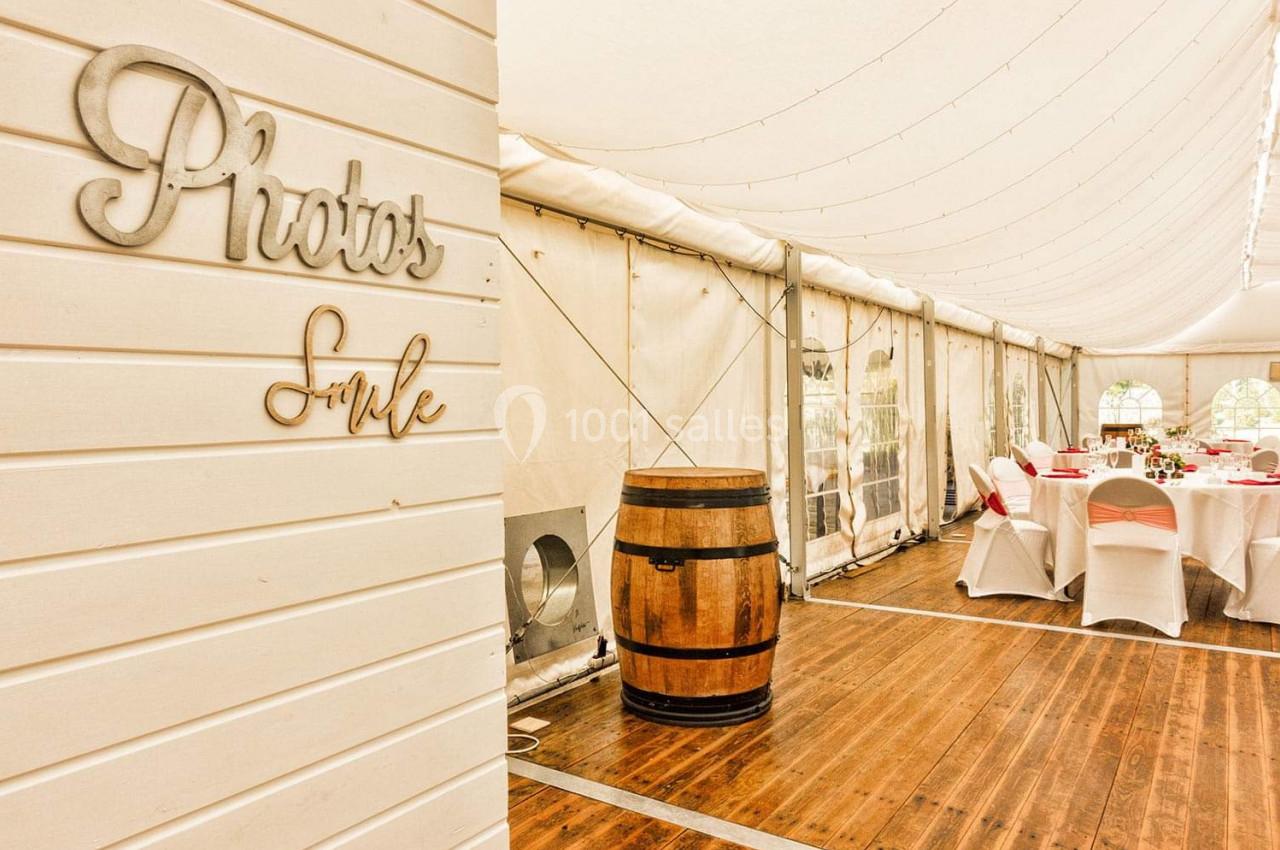 Intérieur d'une tente de réception avec tables dressées, chaises blanches et un tonneau en bois au centre.