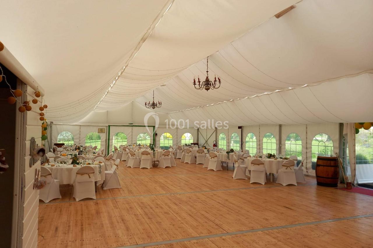 Intérieur d'une tente de réception avec tables dressées, chaises décorées et lustres suspendus.