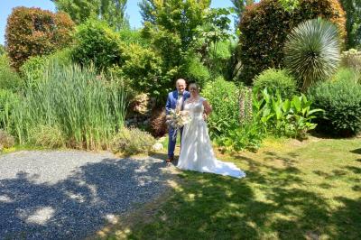 Deux balais déguisés en mariés avec robe et costume, posés devant une tente blanche et un cadre décoratif.