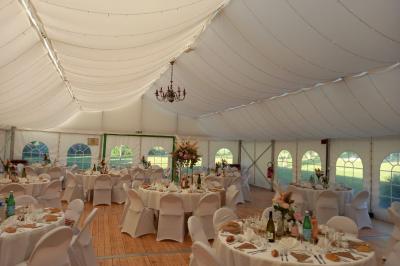 Deux balais déguisés en mariés avec robe et costume, posés devant une tente blanche et un cadre décoratif.