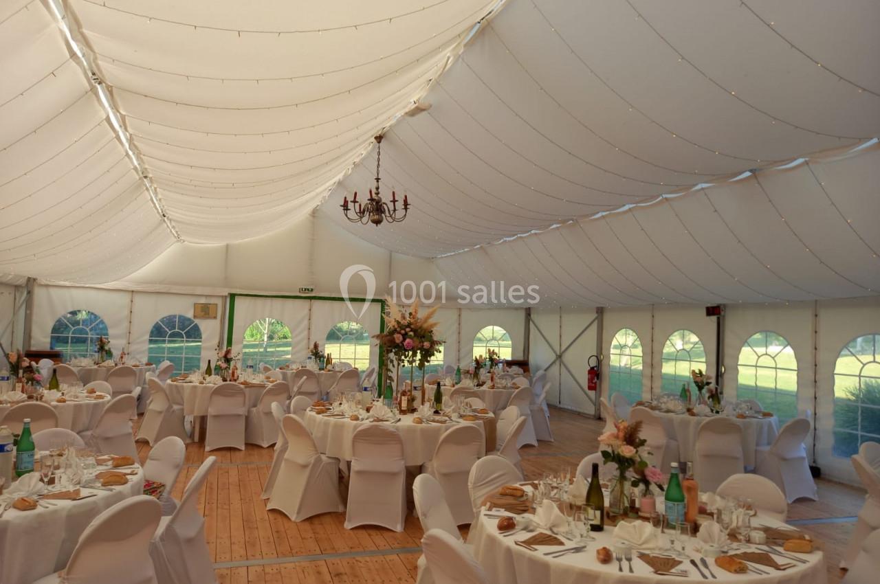 Intérieur d'une tente de réception décorée avec des tables rondes dressées, des chaises blanches et des fleurs.