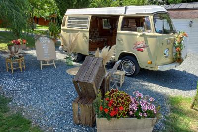 Deux balais déguisés en mariés avec robe et costume, posés devant une tente blanche et un cadre décoratif.