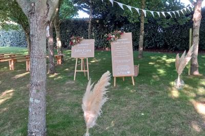 Deux balais déguisés en mariés avec robe et costume, posés devant une tente blanche et un cadre décoratif.