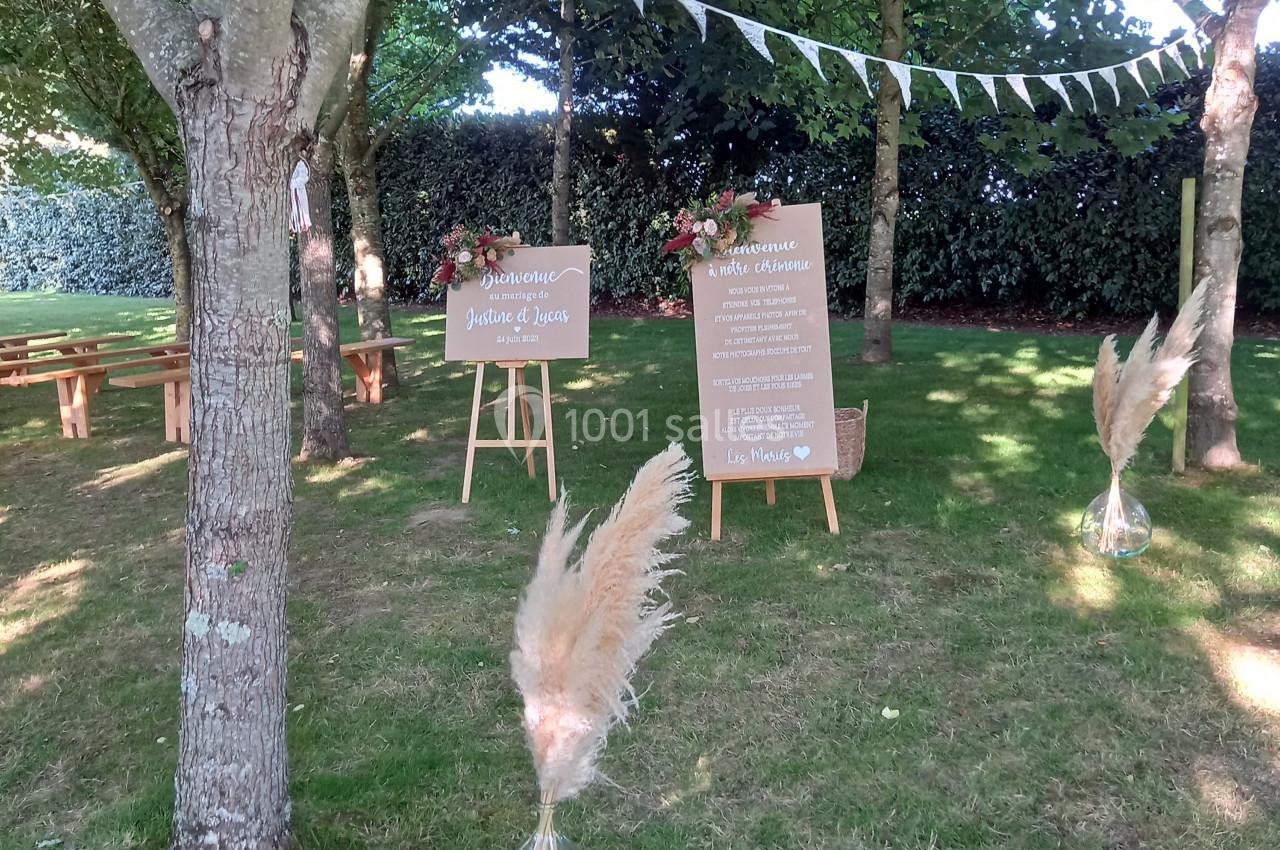 Décoration de mariage en plein air avec panneaux en bois, guirlandes de fanions et herbes de la pampa sous des arbres.