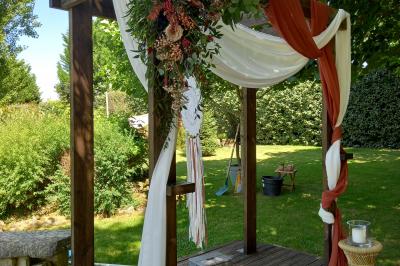 Deux balais déguisés en mariés avec robe et costume, posés devant une tente blanche et un cadre décoratif.