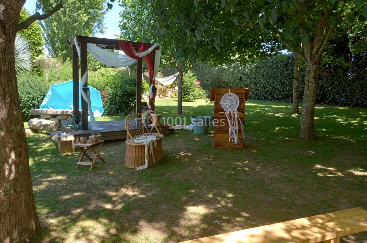 Espace extérieur ombragé avec arche décorée, chaises en bois, panier en osier et éléments de décoration bohème.