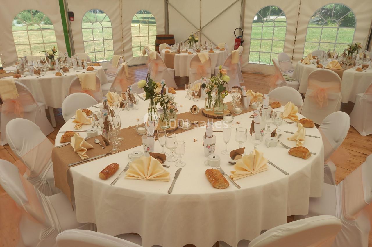 Tables rondes décorées pour un repas festif, avec nappes blanches, serviettes pliées et centres de table fleuris.