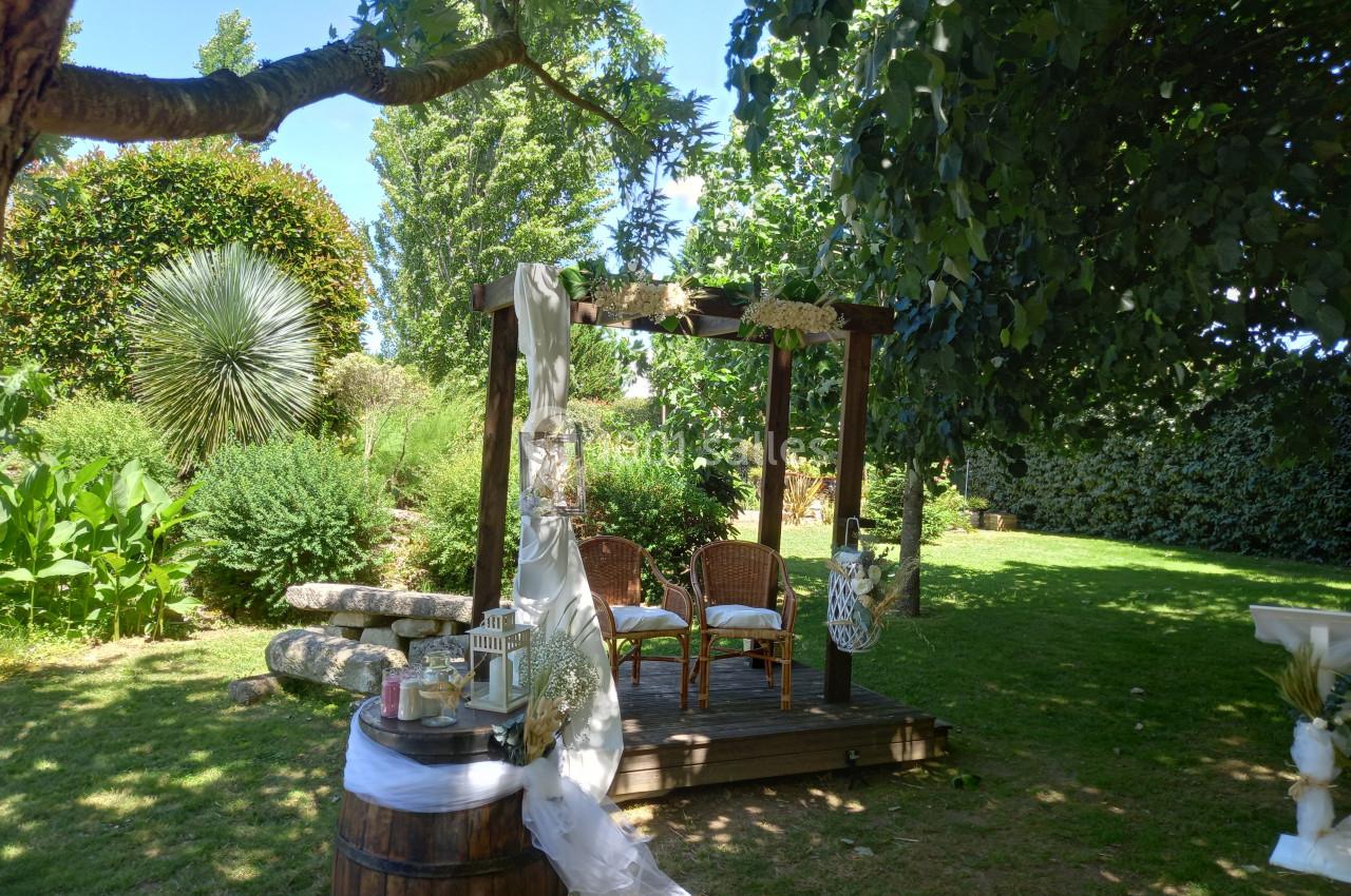 Pergola en bois décorée pour une cérémonie en plein air, entourée de verdure et d'éléments naturels.