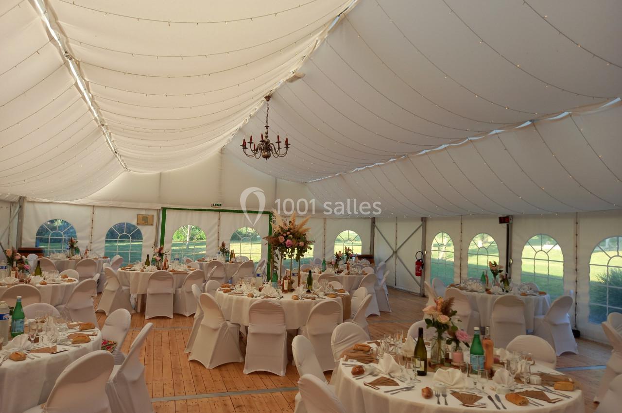 Intérieur d'une tente de réception décorée, avec tables rondes dressées et éclairage doux.