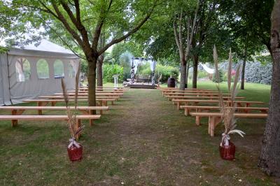 Deux balais déguisés en mariés avec robe et costume, posés devant une tente blanche et un cadre décoratif.